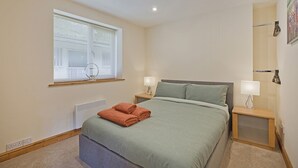 Ein Schlafzimmer mit einem Bett, zwei Nachttischen, einem Fenster mit Jalousien und einer Heizung.