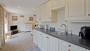 Eine moderne Küche mit weißen Schränken, einer schwarzen Arbeitsplatte, einem Spülbecken, einer Kaffeemaschine und einem Toaster. Auf der Arbeitsplatte ist ein Schild mit der Aufschrift 'REFRESHMENTS'.