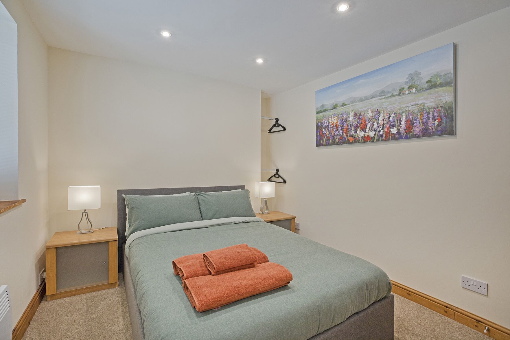 Een slaapkamer met een bed, twee nachtkastjes met lampen, een schilderij aan de muur en een vloerbedekking.