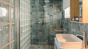 A bathroom with a glass-enclosed shower, a white sink, and a wooden cabinet above the sink. - Aria Blue Suites (Skiathos)