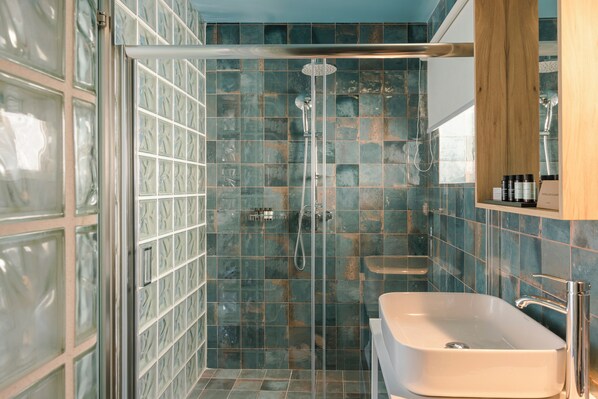 A bathroom with a glass-enclosed shower, a white sink, and a wooden cabinet above the sink. - Aria Blue Suites (Skiathos)