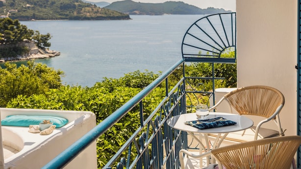 A balcony with a view of a lake, wicker chairs, a small table, and a blue railing. - Aria Blue Suites (Skiathos)