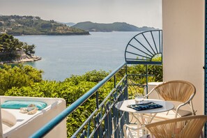A balcony with a view of a lake, wicker chairs, a small table, and a blue railing. - Aria Blue Suites (Skiathos)