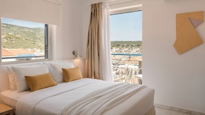 A hotel room with a large bed, a view of the city, and a balcony with outdoor seating. - Aria Blue Suites (Skiathos)