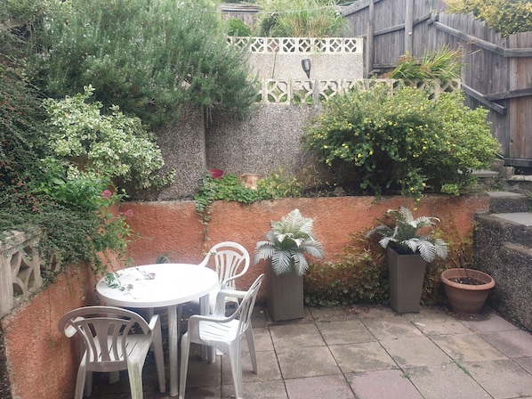 A patio with a round table and four chairs, surrounded by potted plants and a decorative fence.