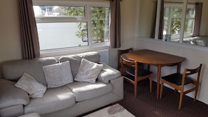 A living room with a sofa, two wooden chairs, a small table, and a window with curtains.