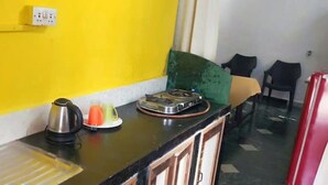 A kitchen with a yellow wall, a kettle, a plate with fruit, and a stove. - Alexmarie Holiday Home  (5) nr Candolim Beach  (Bardez Candolim)