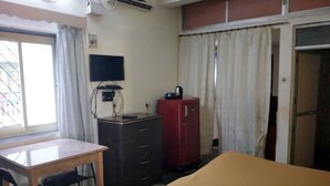 A hotel room with a bed, a desk, a chair, a wardrobe, a television, and a window with curtains. - Alexmarie Holiday Home  (5) nr Candolim Beach  (Bardez Candolim)