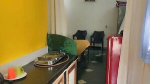 A narrow kitchen with a gas stove, a sink, and a refrigerator. There are two chairs and a table in the adjacent dining area. - Alexmarie Holiday Home  (5) nr Candolim Beach  (Bardez Candolim)