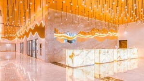 A modern lobby with a marble reception desk, hanging lights, and a wavy wall design.