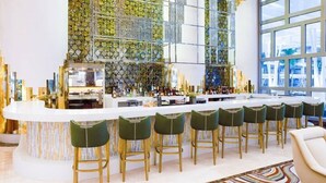 A modern bar area with a white countertop, green bar stools, and a decorative wall with a geometric pattern.