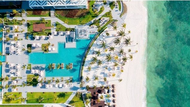 An aerial view of a resort with a pool, beach, and palm trees.