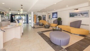 A modern hotel lobby with a reception desk, seating areas, and a large window with a view of the ocean. - Residence Pierre & Vacances Audierne le Phare de Trescadec (Audierne)