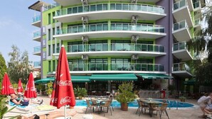 Un hotel de varios pisos con piscina al aire libre, sillones de descanso y zona de comedor con sombrillas.