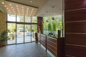 A reception area with a glass door leading outside, a reception desk, and potted plants. - Hotel L&B Sunny Beach (Nessebar)