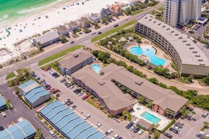 Vue aérienne d’un hôtel situé sur la côte, composé de plusieurs bâtiments, avec une plage et une piscine.