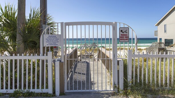 A gated entrance to a private beach property with a sign indicating video surveillance.