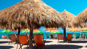 Ein Strand mit Reetsonnenschirmen und Holzkunststühlen.