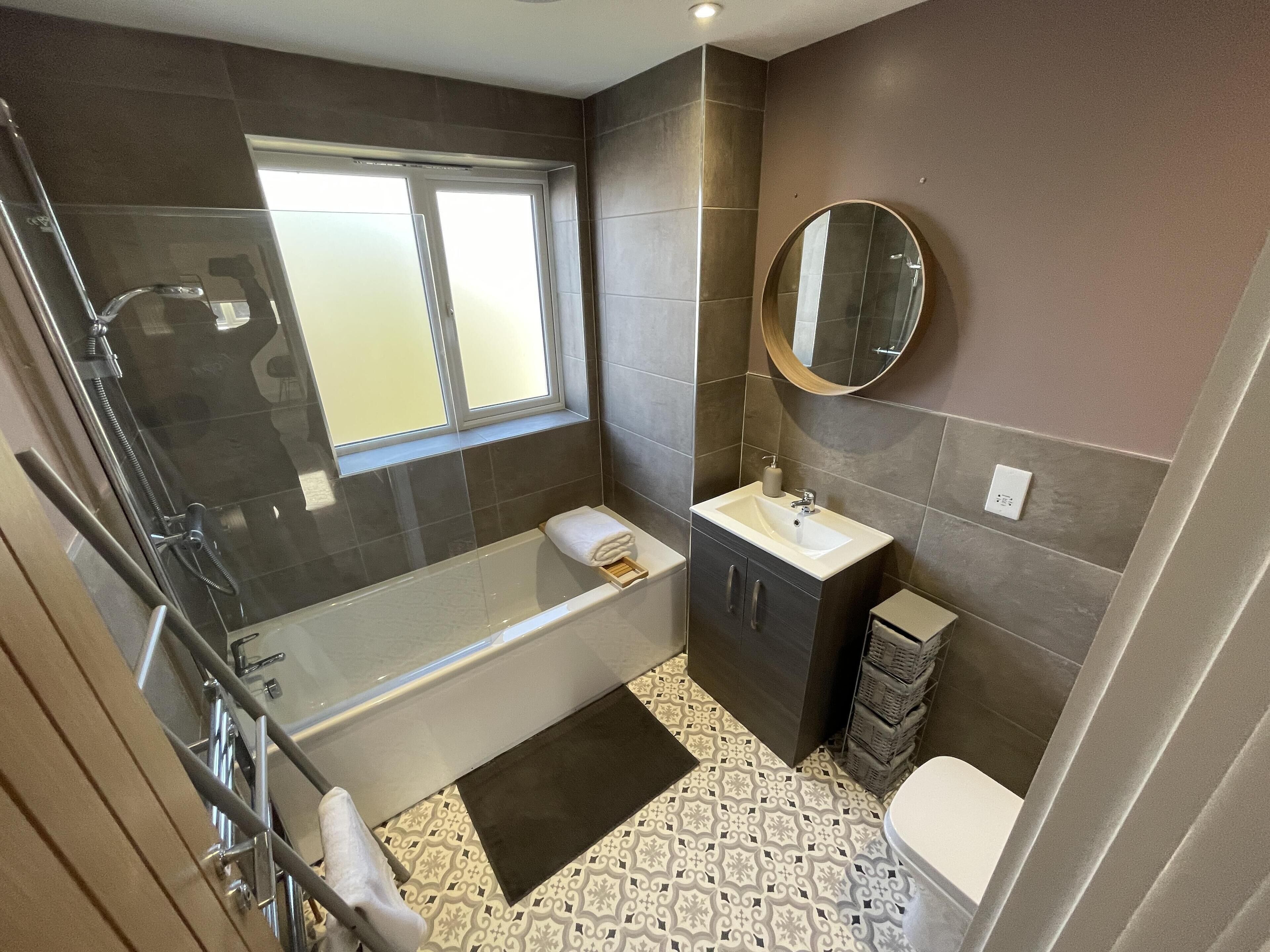 A modern bathroom with a glass-enclosed shower, a vanity with a mirror, and patterned floor tiles.