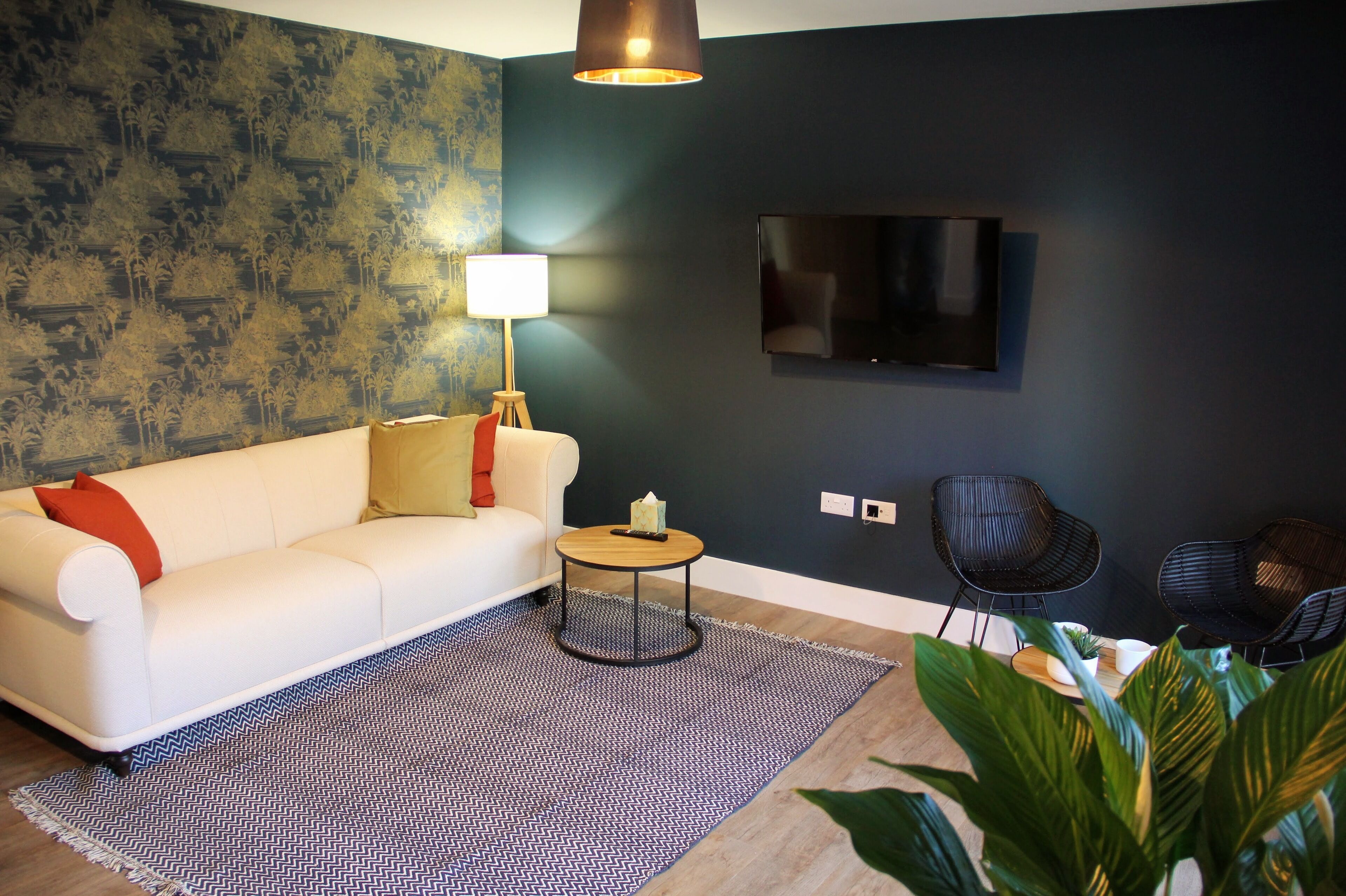 A modern living room with a white sofa, a round coffee table, two black chairs, a TV mounted on the wall, and a patterned rug.