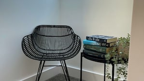 Una habitación de esquina con tragaluz, una silla negra tejida, una mesita con libros y una planta en maceta.