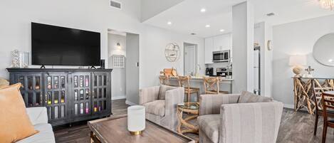 A spacious living room with a flat-screen TV, dark wood flooring, and a ceiling fan.
