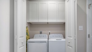 A laundry room with two white front-loading washers and dryers, white cabinets above, and a yellow towel hanging on the left wall. - Little's Toasty Coasty by Miss Kitty’s (Rockport)