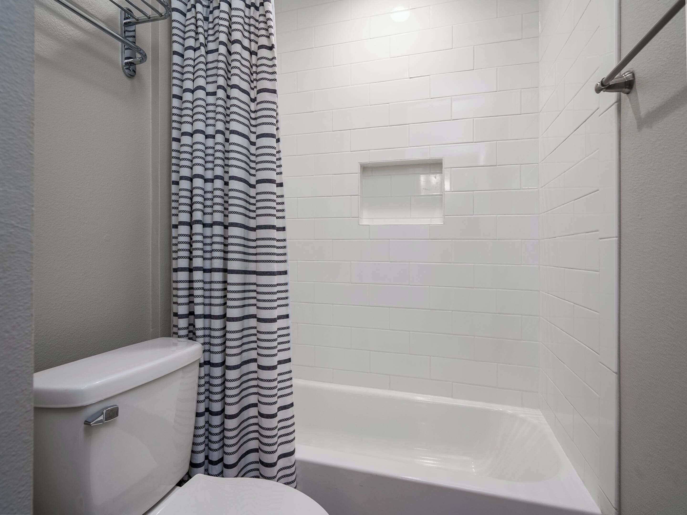 A bathroom with a white bathtub, a toilet, and a shower curtain with a black and white pattern.