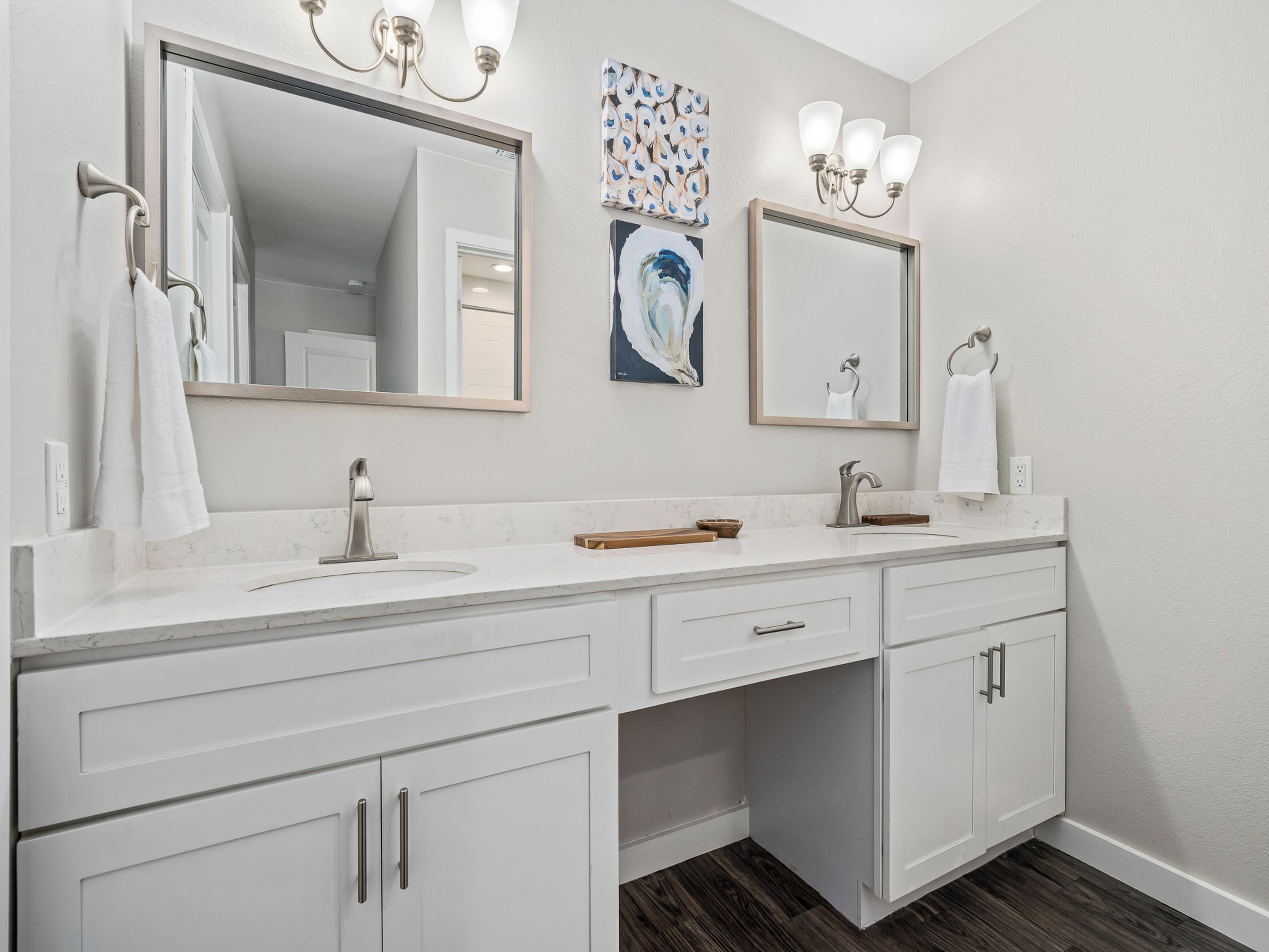 Un baño moderno con tocador blanco, dos espejos, lavamanos y ducha.