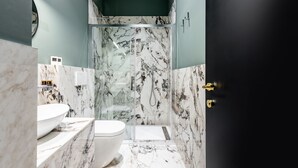 Une salle de bain dotée d’une douche à parois de verre, de toilettes blanches et de plans de toilette en marbre.