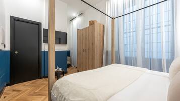 Ein modernes Schlafzimmer mit einem großen Bett, einem Holzschrank, einem kleinen Tisch mit einer Lampe und Blick auf die Stadt durch transparente Vorhänge.