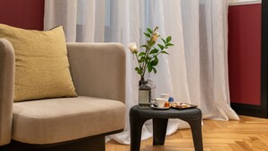 Un salon moderne avec un canapé beige, une petite table noire ornée d’un vase de fleurs blanches, une tasse et une assiette de nourriture.