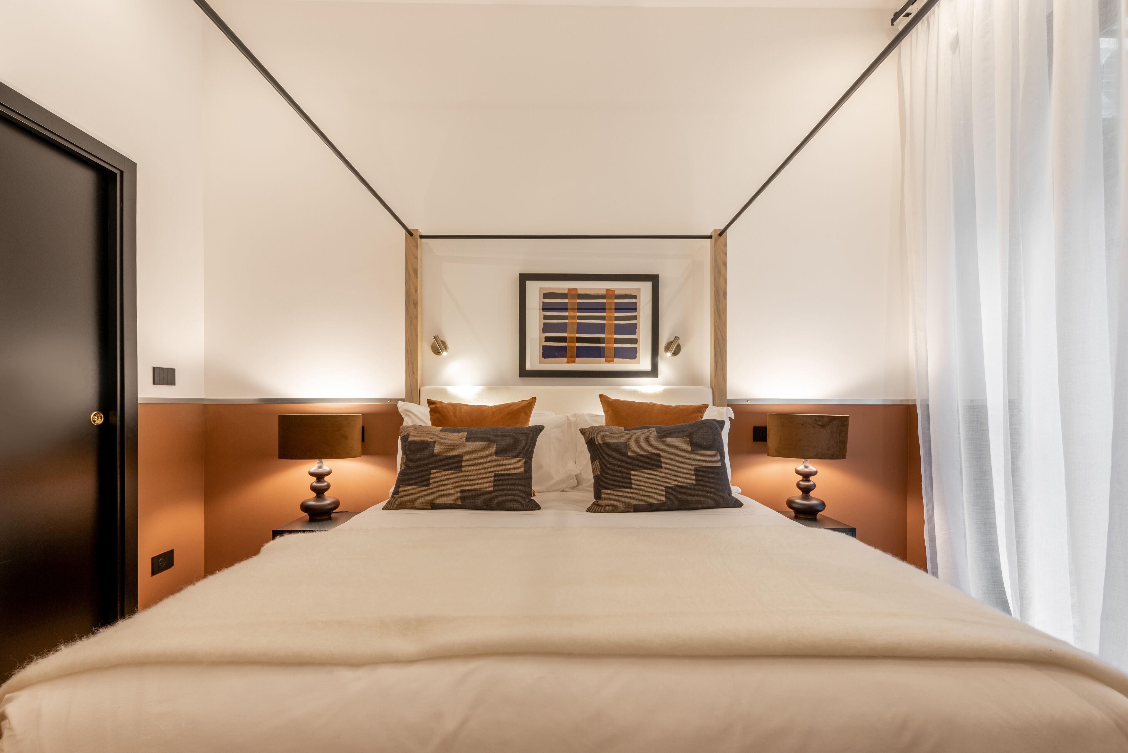 Ein Hotelzimmer mit einem großen Bett, zwei Nachttischen mit Lampen, einem gerahmten Bild an der Wand und einer Tür.
