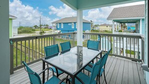 A covered outdoor area with a glass-top table and blue chairs, overlooking a residential neighborhood. - Sandy Pants Beach House by Miss Kitty’s (Rockport)