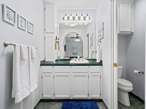 A bathroom with a white vanity, a sink, and a toilet. There are towels hanging on a rack, a blue rug on the floor, and a mirror above the sink.