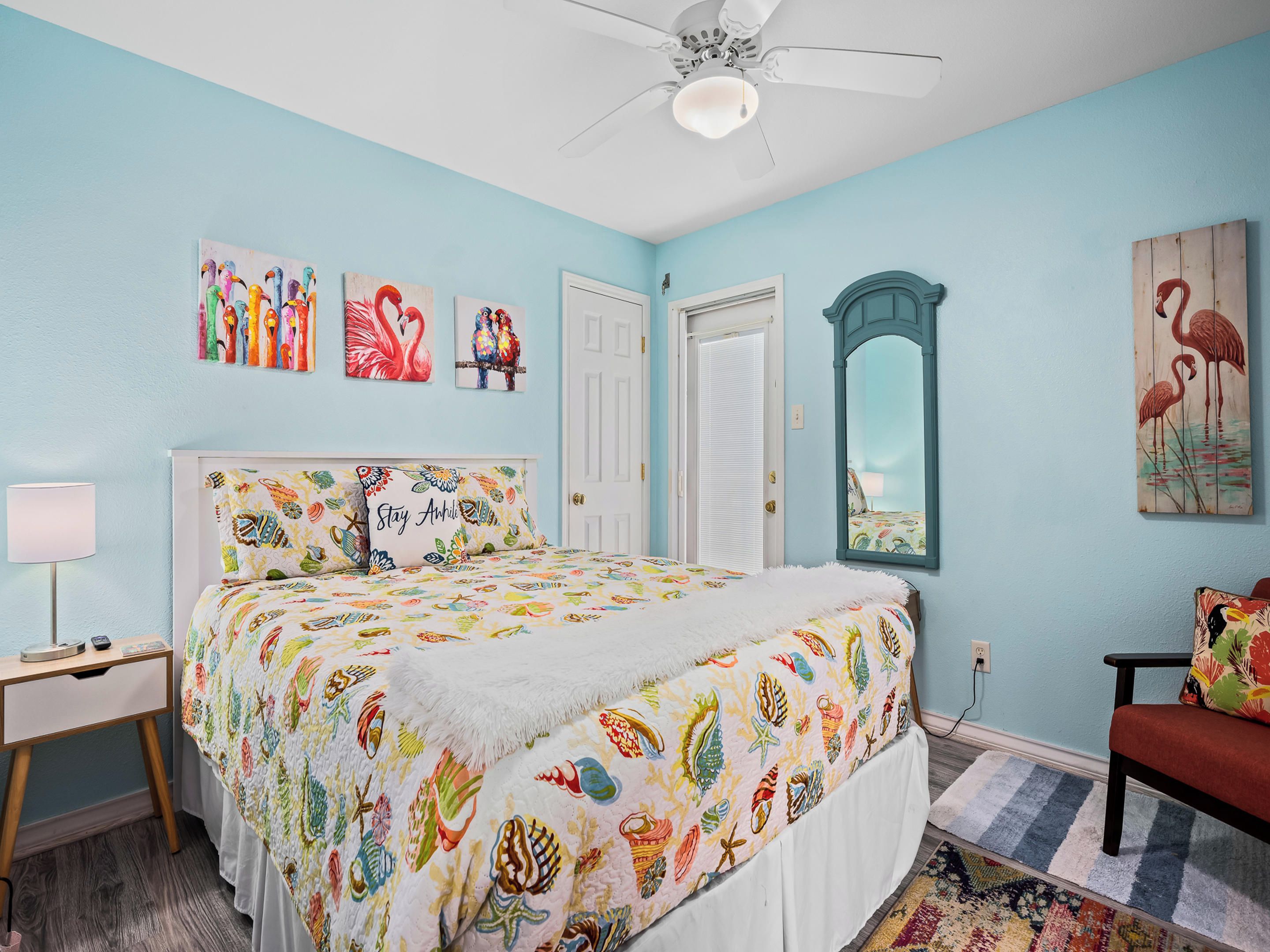 A bedroom with a bed, a desk, a chair, a mirror, and artwork on the walls.
