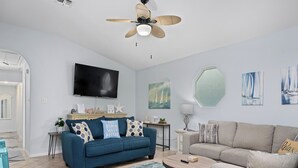 A modern living room with a blue sofa, a grey sofa, a round coffee table, and a ceiling fan. - Sandy Pants Beach House by Miss Kitty’s (Rockport)