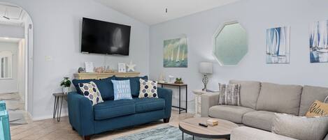 A modern living room with a blue sofa, a grey sofa, a round coffee table, and a ceiling fan.