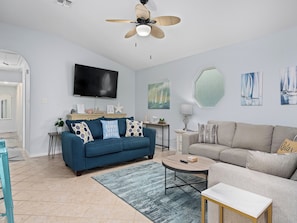A modern living room with a blue sofa, a grey sofa, a round coffee table, and a ceiling fan. - Sandy Pants Beach House by Miss Kitty’s (Rockport)