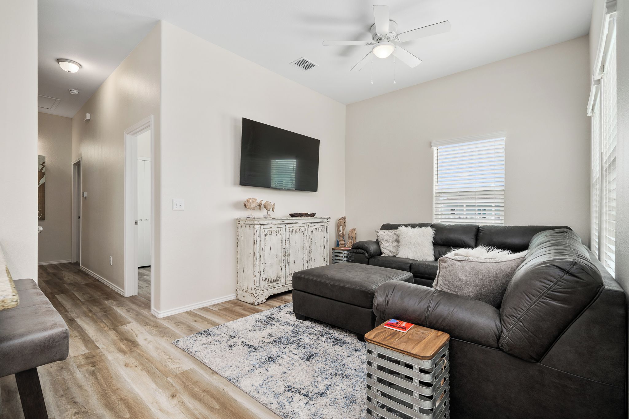 A modern living room with a dark leather sofa, a wooden coffee table, and a white cabinet with decorative items.