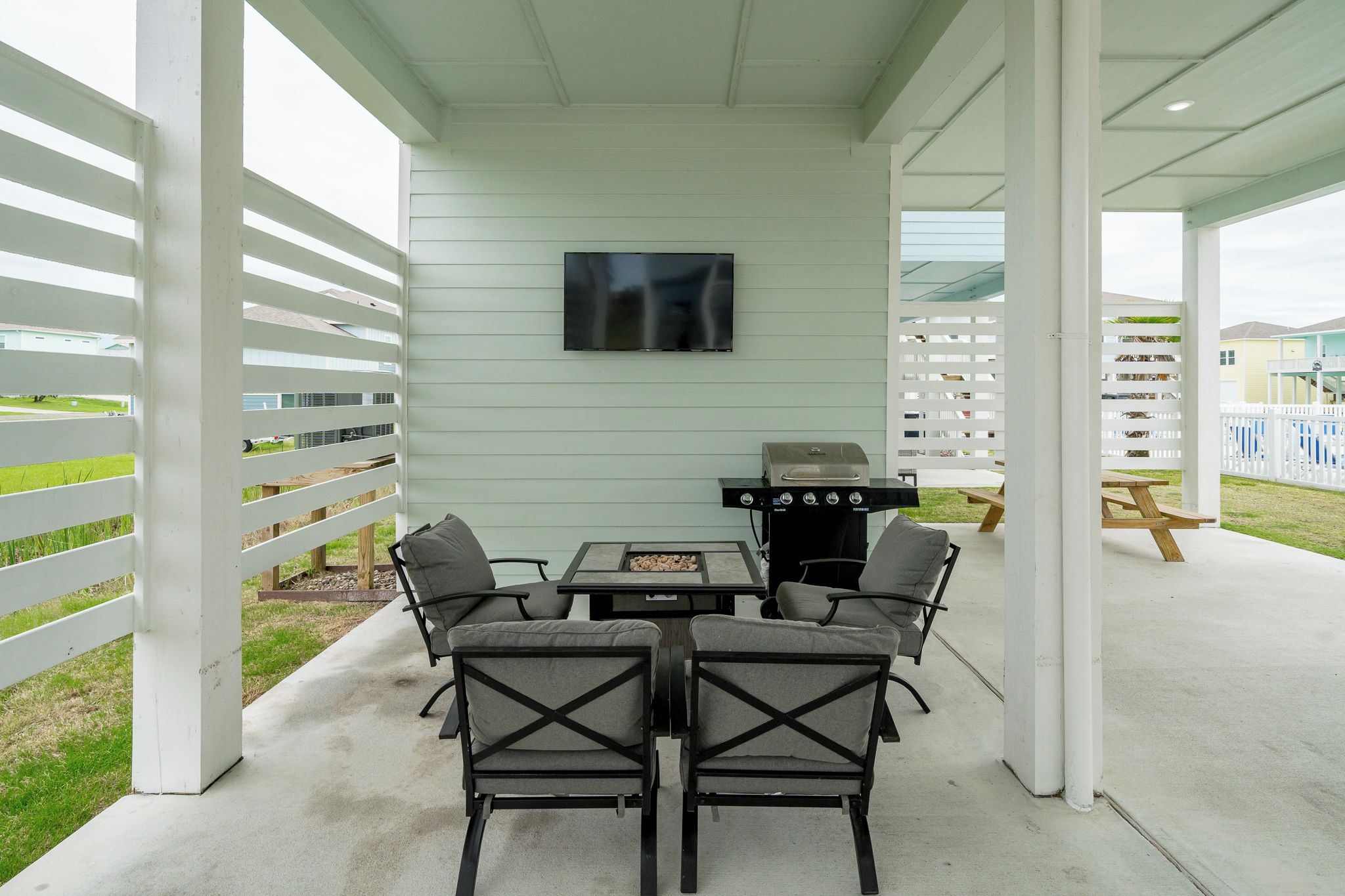 Une terrasse extérieure équipée d’un barbecue, de sièges et d’un téléviseur fixé au mur.