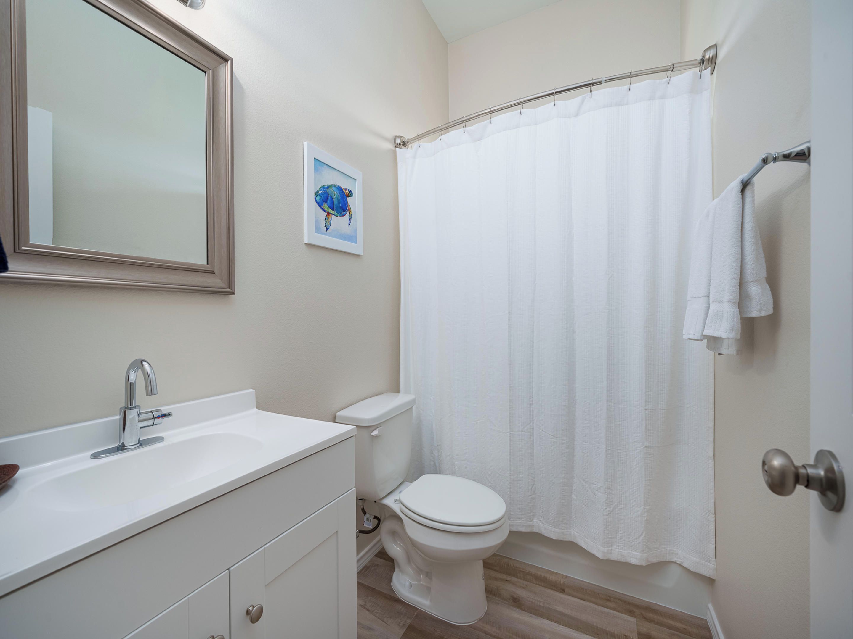 A bathroom with a white sink, a toilet, a shower curtain, and a framed picture on the wall.