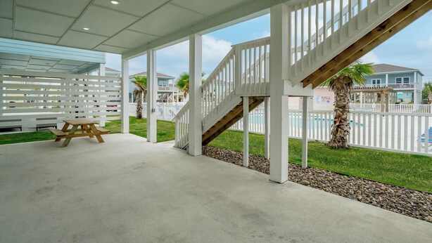 Un espace extérieur abrité, doté d’une table de pique-nique, de rampes blanches et d’un escalier menant à une zone de piscine.