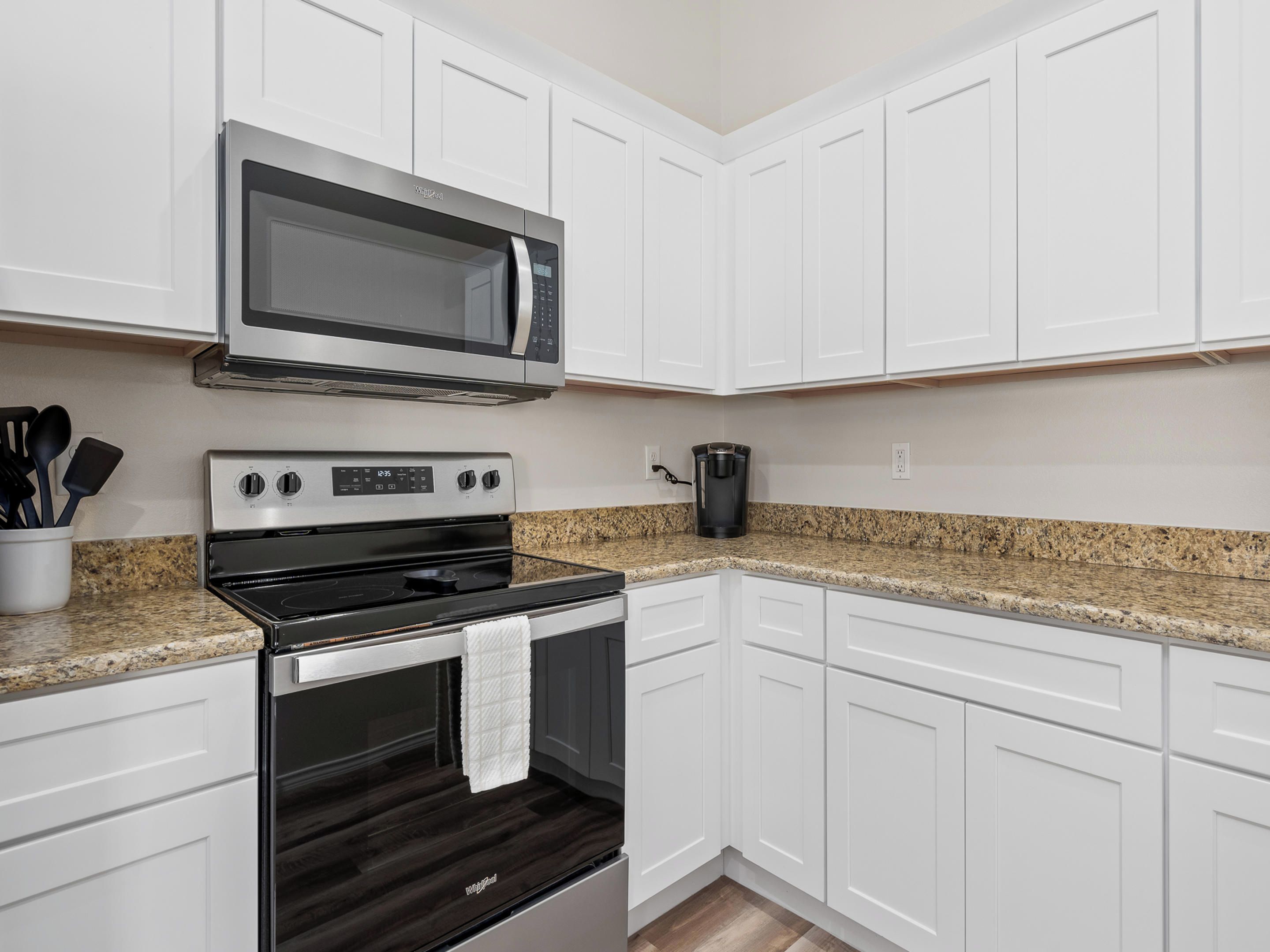A kitchen with white cabinets, a microwave, a stove, and a coffee maker.