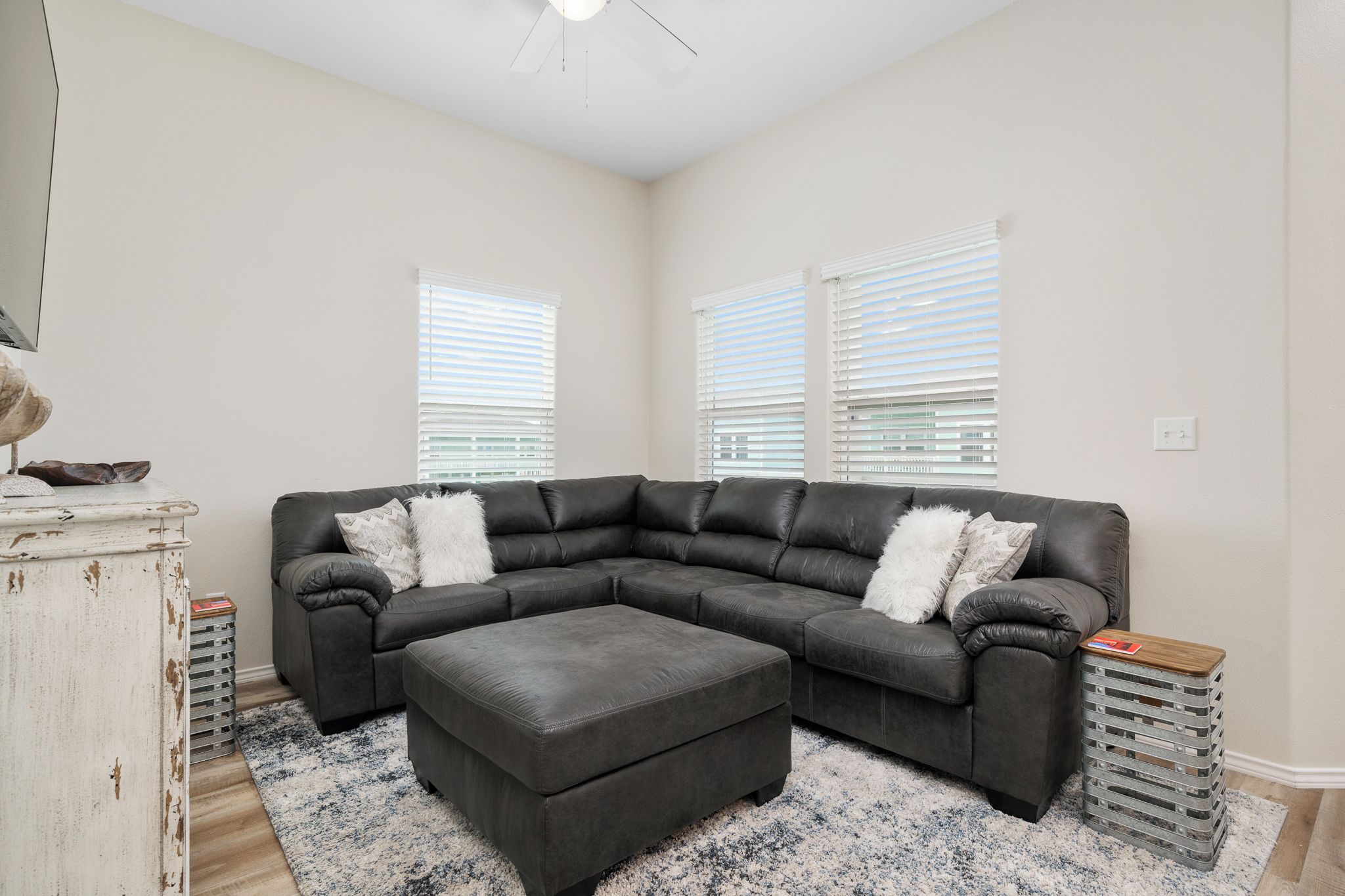 A living room with a sectional sofa, ottoman, and a rustic white dresser.