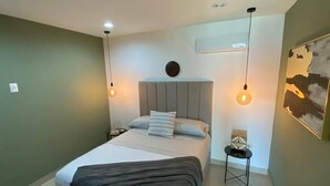 A bedroom with a bed, bedside tables, a wall-mounted air conditioner, and a painting on the wall. - CONDOS ONE ByTrvl2hm & Mazatlan Regency (Mazatlán)