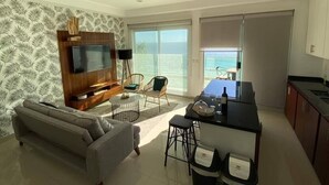 A modern living room with a sofa, TV, and dining area. - CONDOS ONE ByTrvl2hm & Mazatlan Regency (Mazatlán)