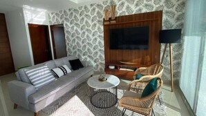 A living room with a sofa, two armchairs, a coffee table, a TV, and a patterned wall. - CONDOS ONE ByTrvl2hm & Mazatlan Regency (Mazatlán)