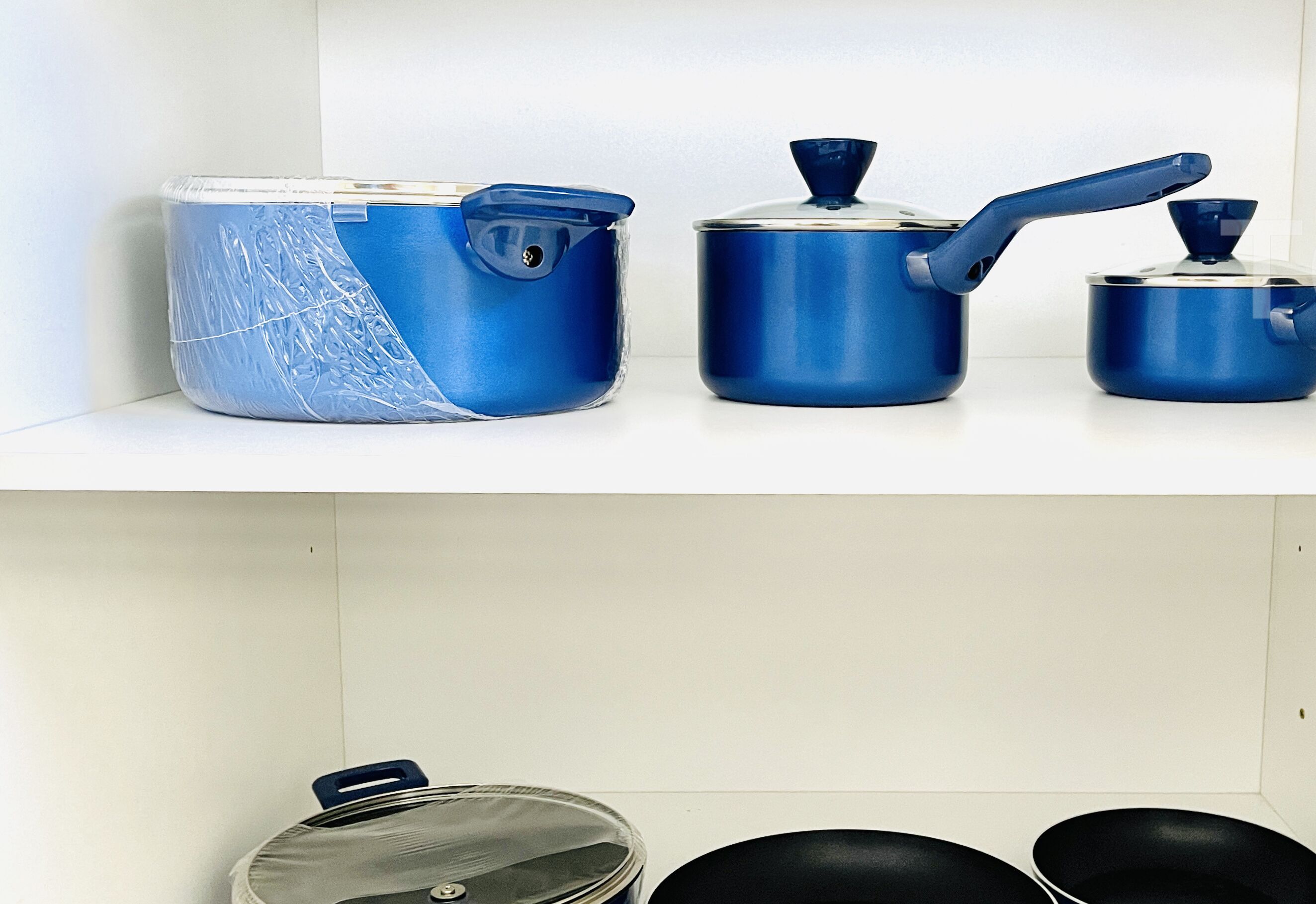 Una cocina con tres ollas y sartenes azules sobre un estante blanco.