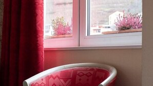 A room with a bed, a window with a view of a landscape, and a chair with a patterned cushion. - The Originals City, Hotel de L'ange, Guebwiller (Guebwiller)